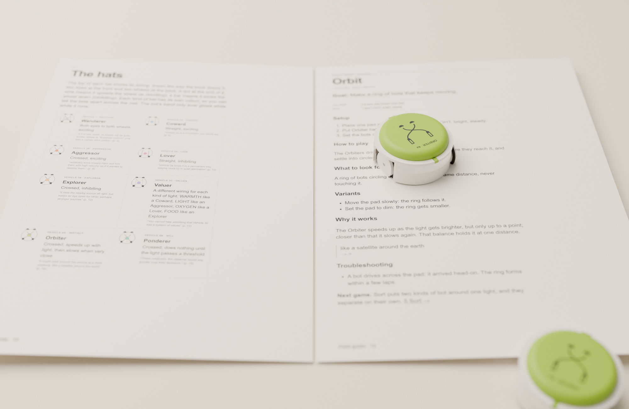The field guide open on the felt at the Orbit page, two green Orbiter bots beside it.